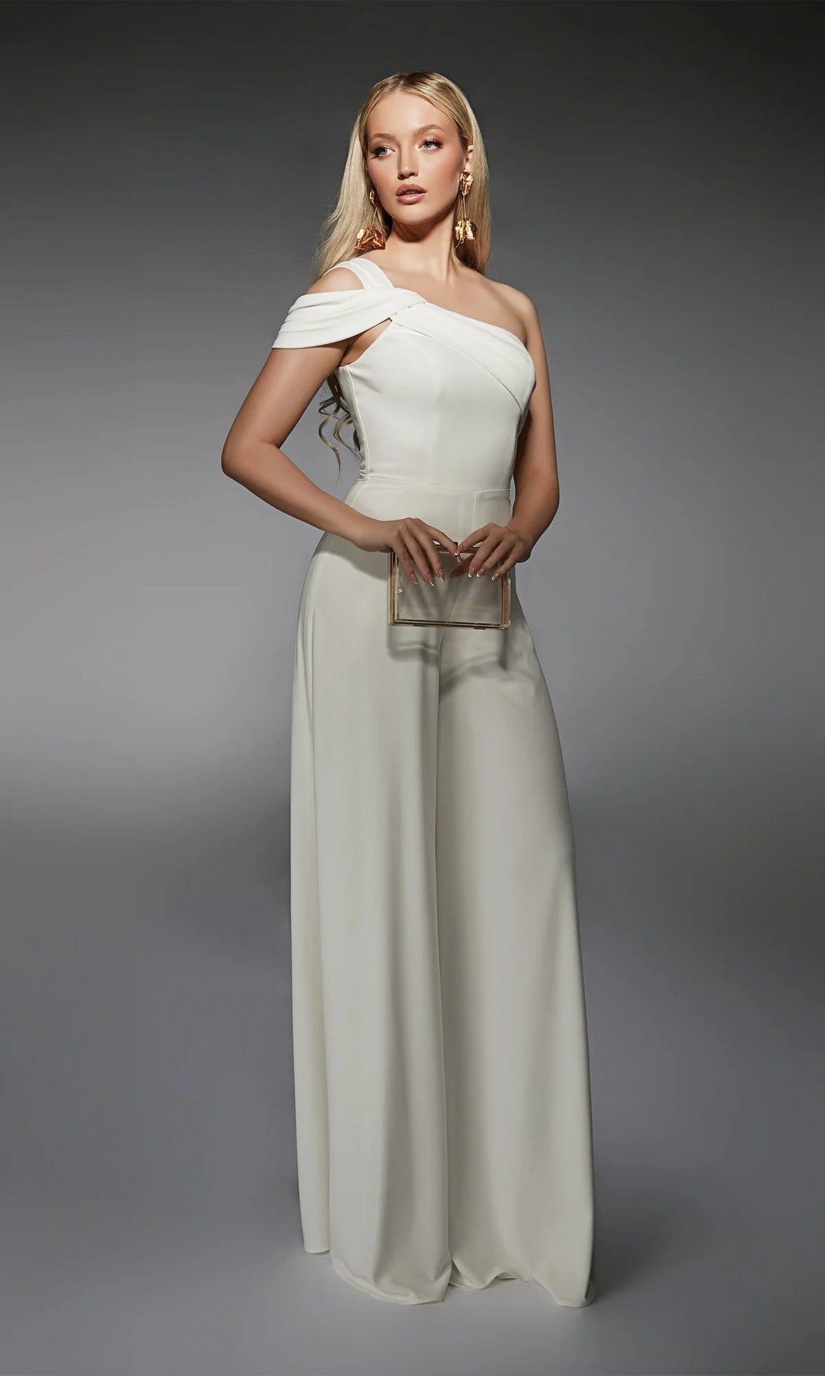 A woman stands against a gray background wearing the Alyce 70066 Long Formal Jumpsuit, featuring a white one-shoulder design with wide-leg pants, and holds a clear rectangular clutch.